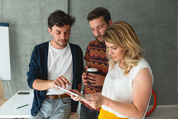 Trzy osoby w biurze patrzące wspólnie na tablet podczas rozmowy lub pracy zespołowej