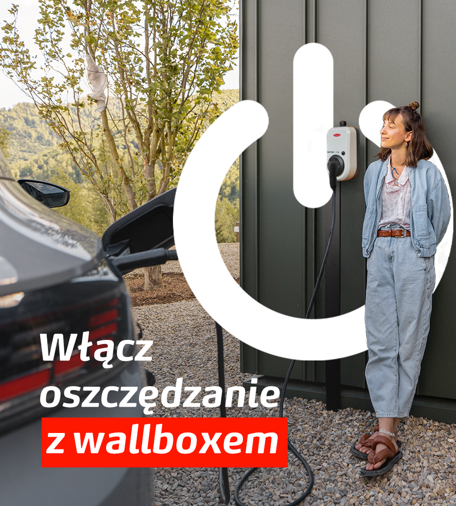 Młoda kobieta uśmiecha się, stojąc obok wallboxa do ładowania samochodów elektrycznych. Biały symbol włącznika energii jest nałożony na obraz. Obok znajduje się tekst: Włącz oszczędzanie z wallboxem. W tle widać podłączony samochód elektryczny i zieleń.