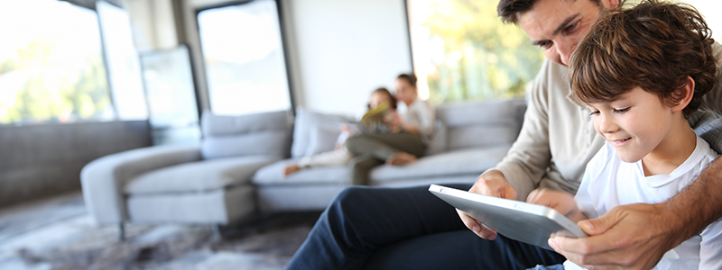 Rodzina relaksuje się w salonie. Tata z synem korzysta z internetu na tablecie.