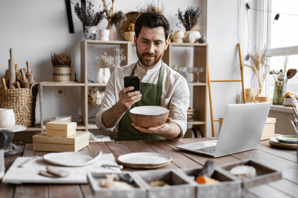 Mężczyzna w fartuchu fotografujący telefonem ceramiczną misę w pracowni rękodzieła